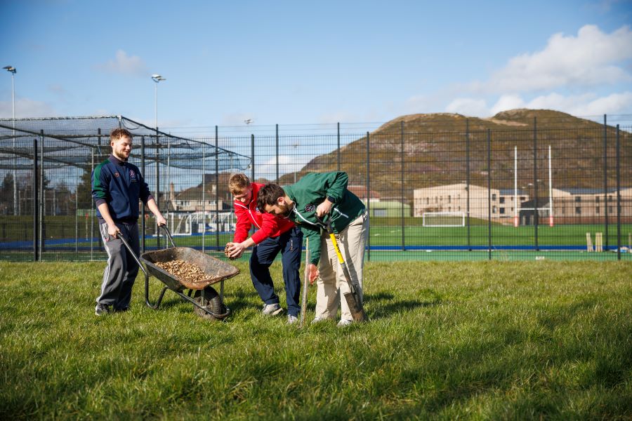 Student athletes with a wheelbarrow at Peffermill Playing Fields with Arthurs Seat in the background